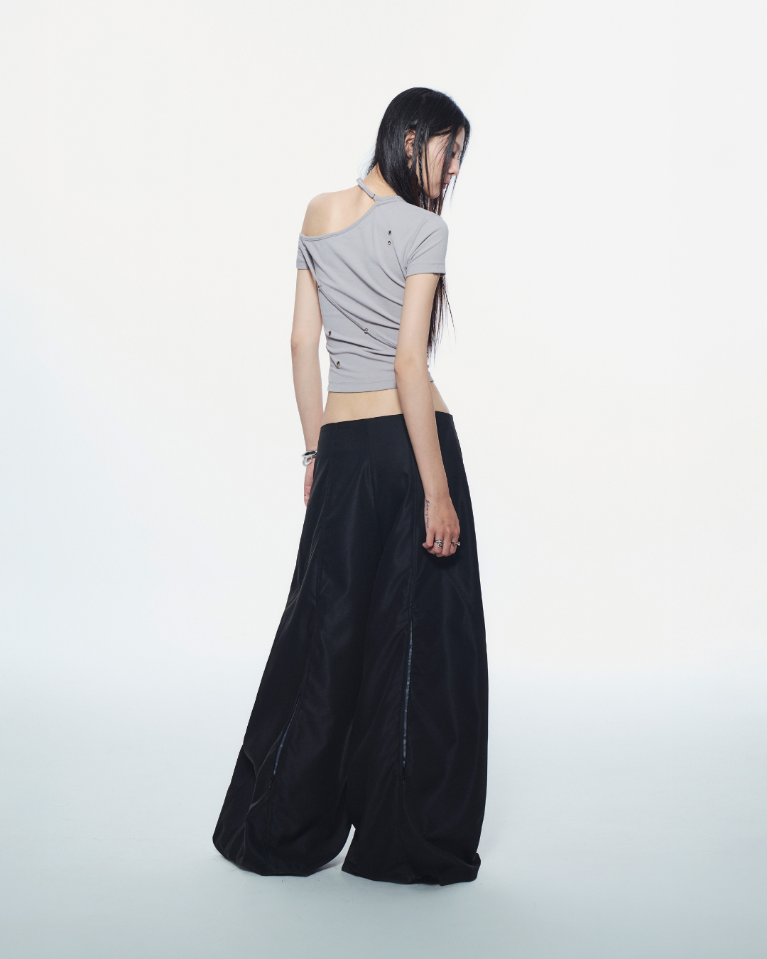 Woman wearing a gray one-shoulder top and black wide-leg pants on a white background