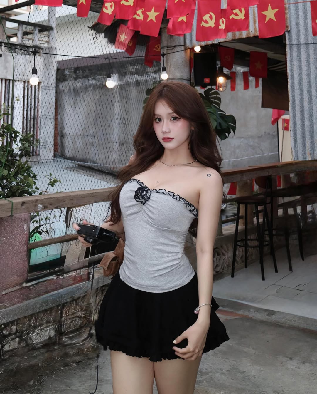 Woman in a gray top and black skirt standing in an outdoor setting with flags in the background