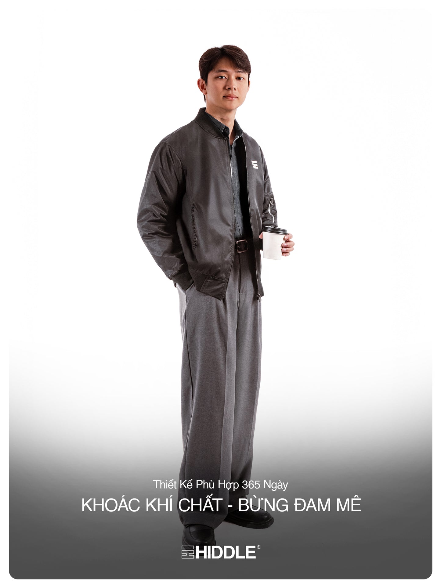 Man wearing a gray outfit with a belt, holding a cup on a white background
