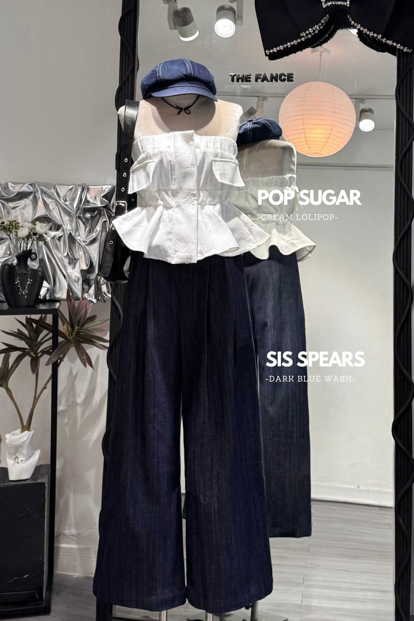 Mannequin wearing a white ruffled top and dark blue pants with visible branding in a store setting.