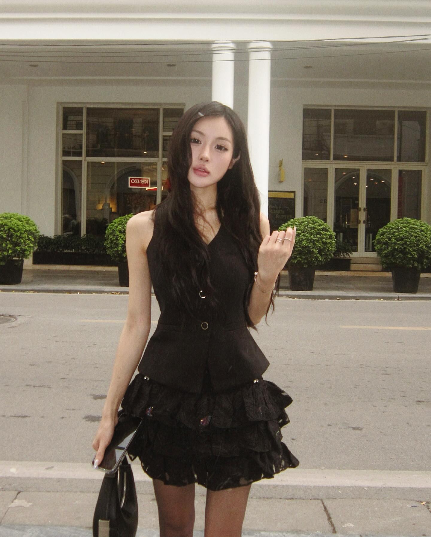 Woman in a black dress standing on a street with a building in the background