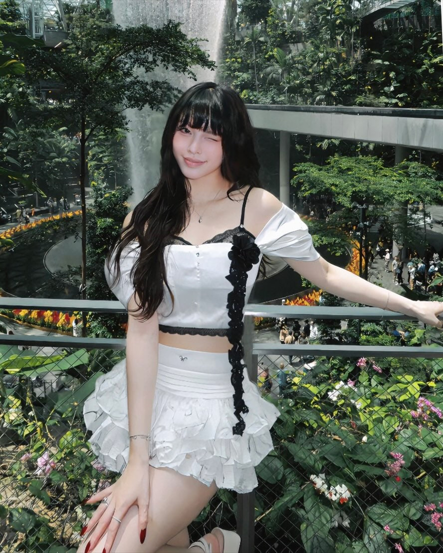Woman in a white outfit with black accents standing in a garden setting