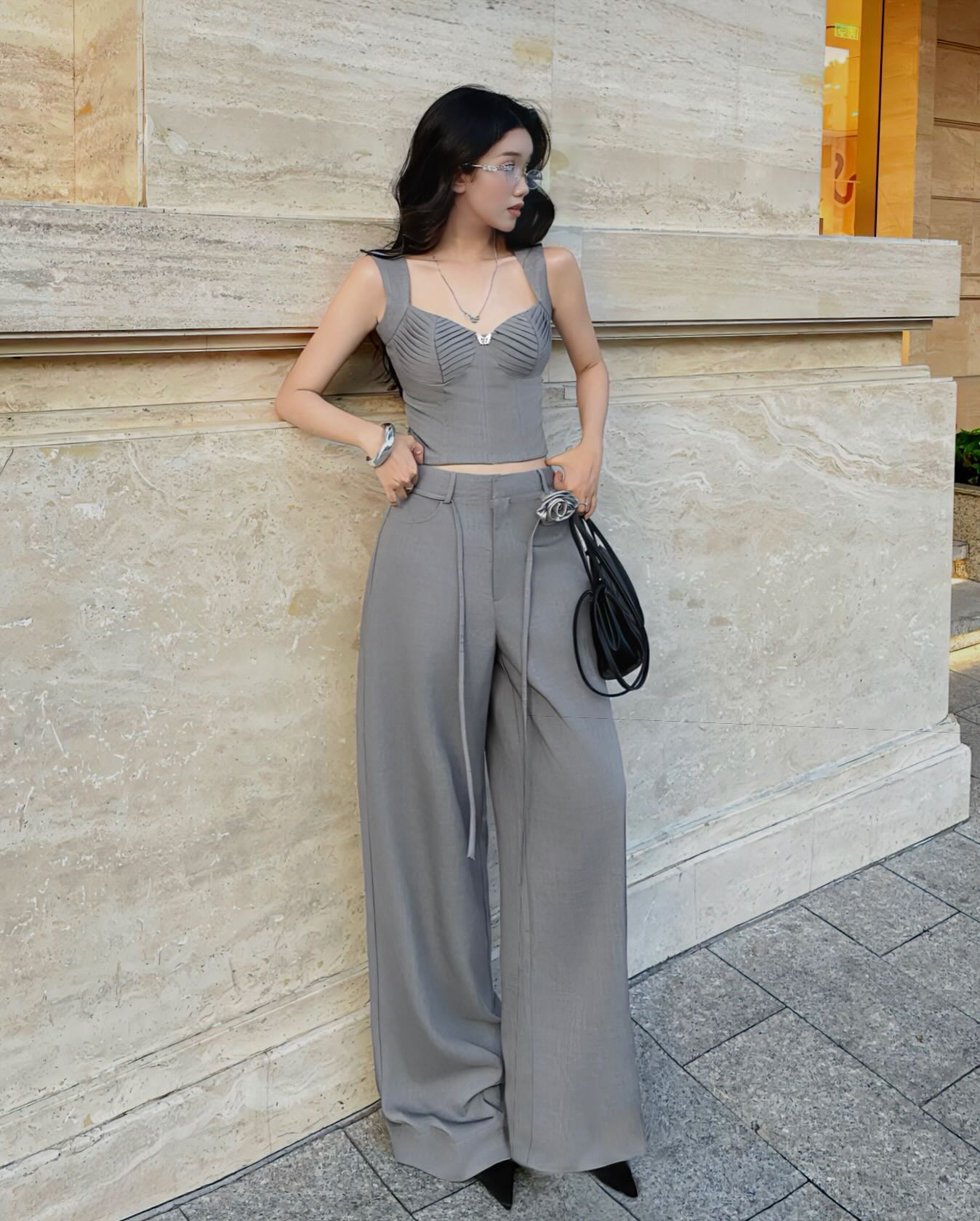 Woman in a gray outfit standing against a stone wall.