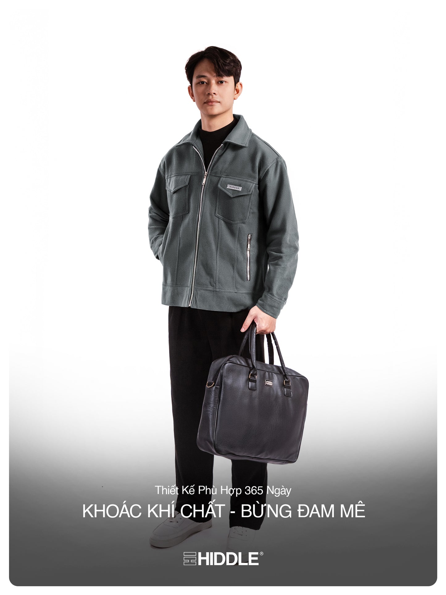 Man holding a black leather bag wearing a gray jacket on a white background