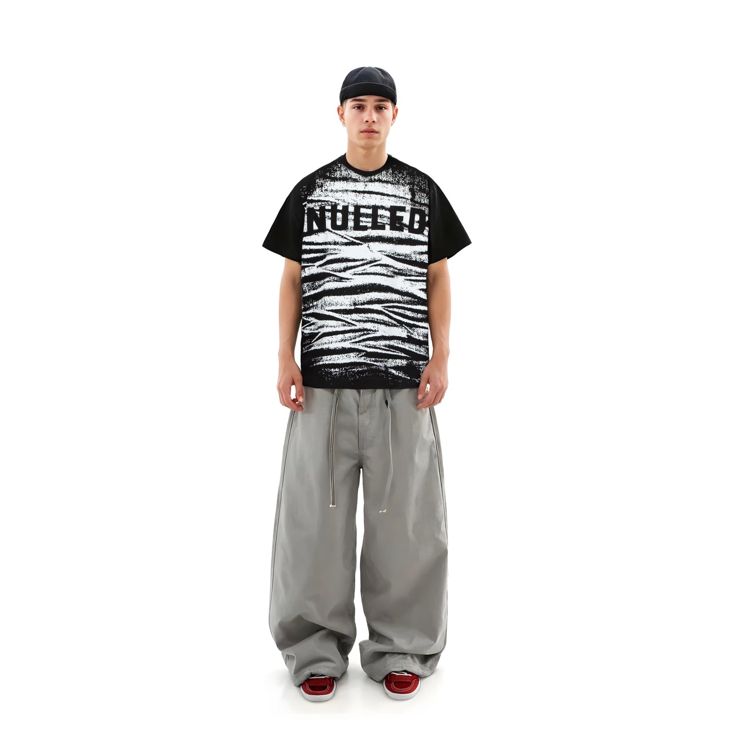 Person wearing a black and white graphic t-shirt with text, gray pants, and red shoes on a white background