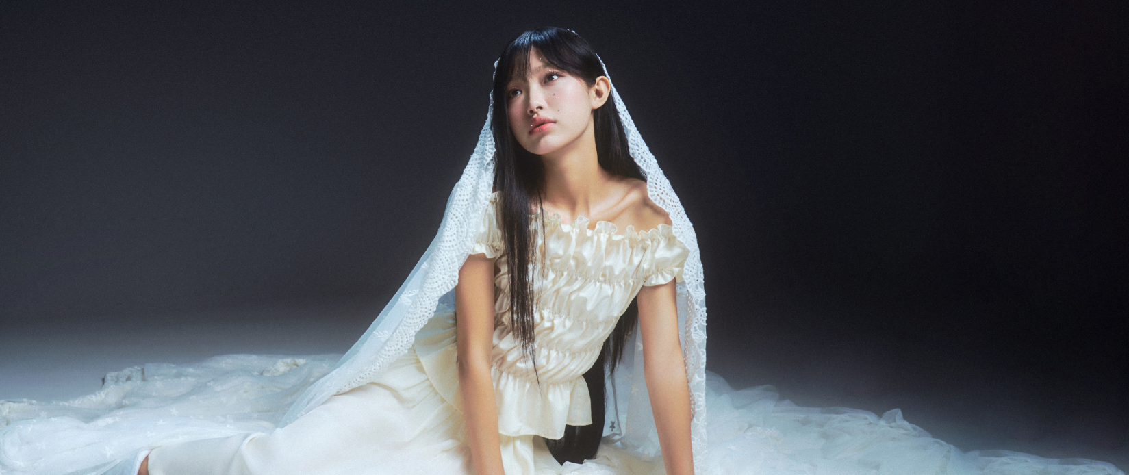 Woman in a white dress sitting on a dark background