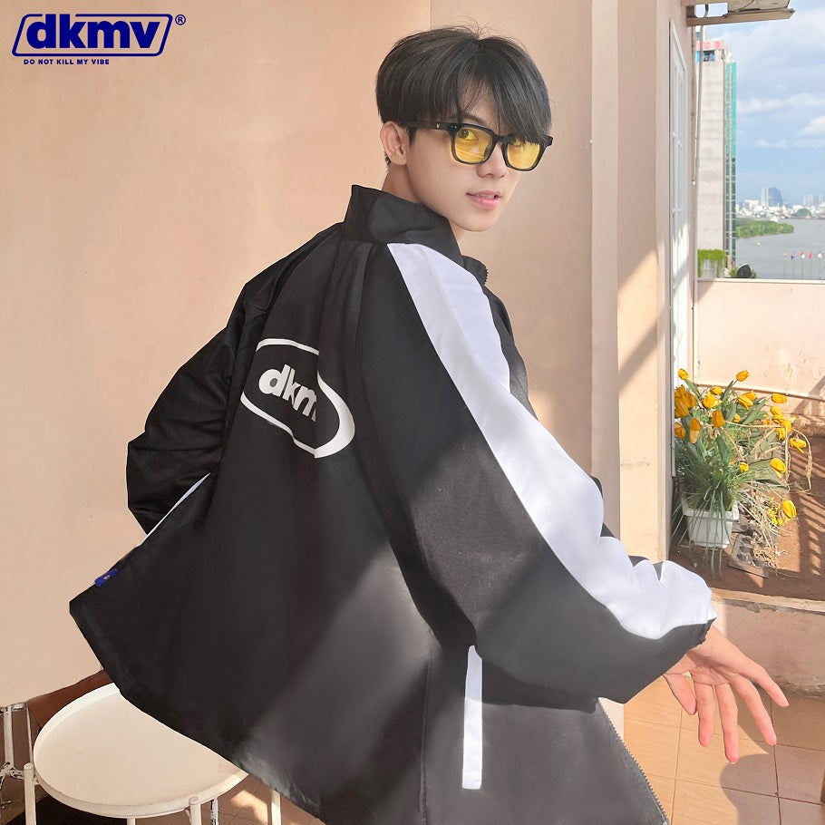 Person wearing a black and white jacket with dkmv logo indoors.