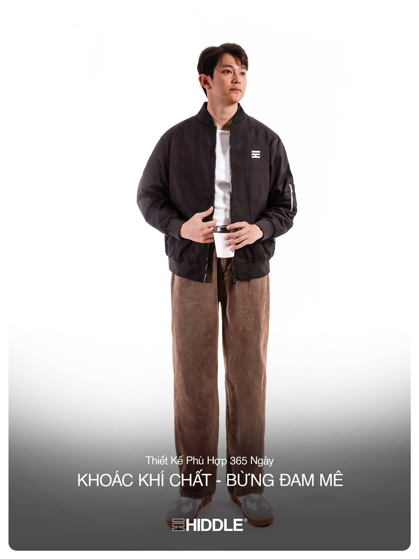 Person wearing a black jacket and brown pants holding a white cup with a logo on a white background