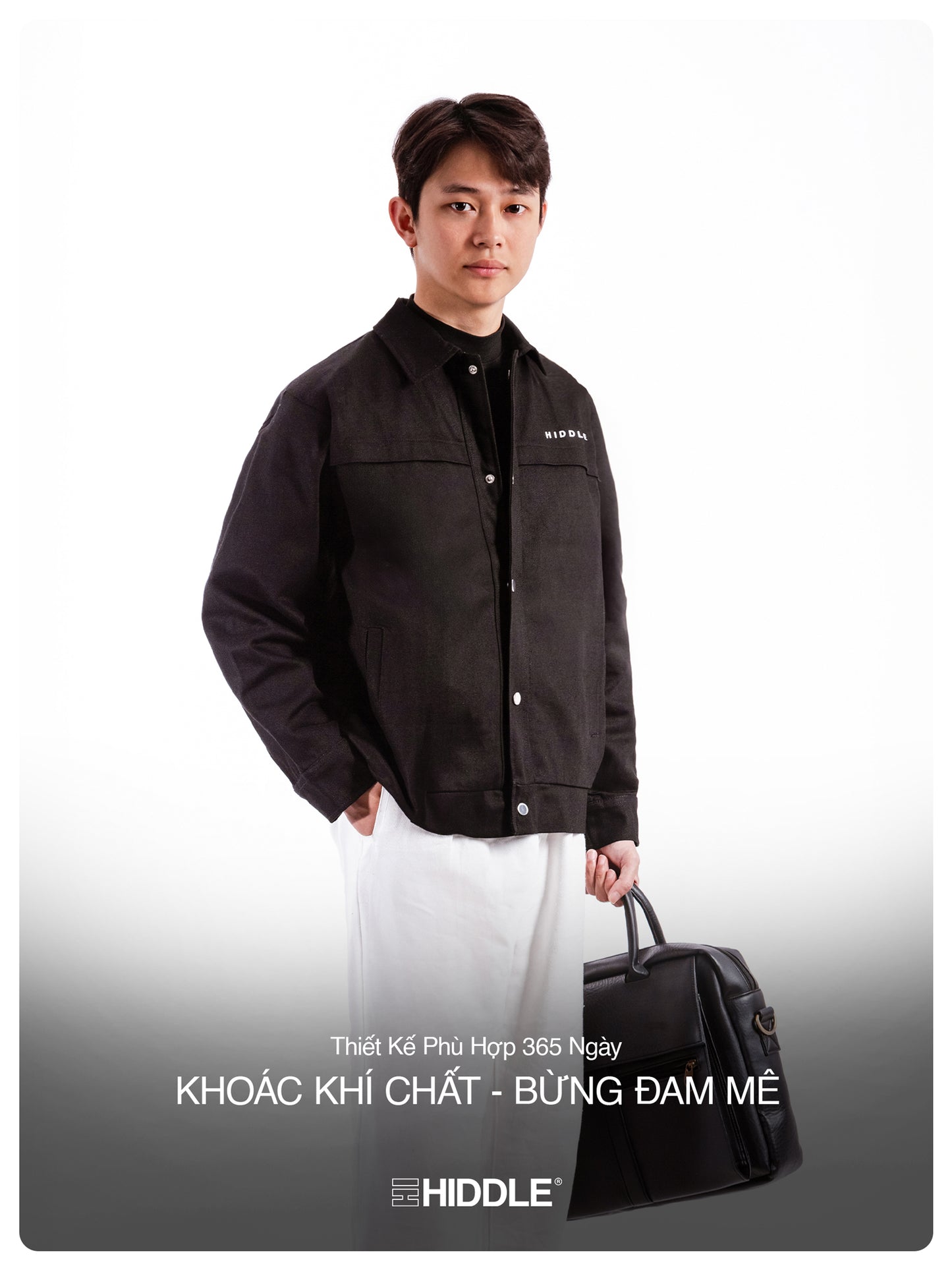 Man wearing a black jacket with a visible brand logo, holding a black bag on a white background.