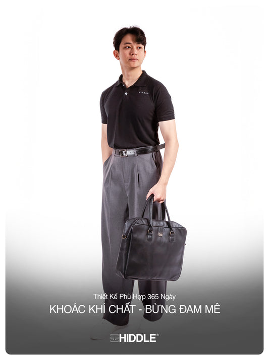 Man holding a black bag wearing a black shirt and gray pants on a white background with Hiddle branding.