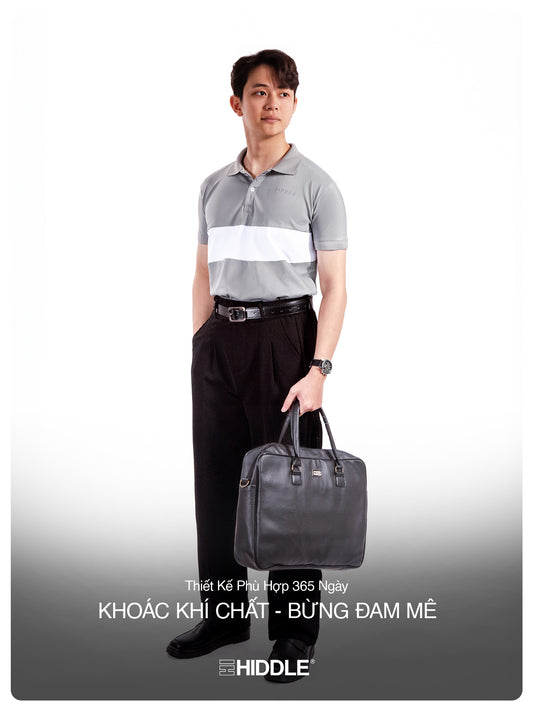 Man holding a black briefcase against a white background, wearing a gray and white polo shirt with black pants.