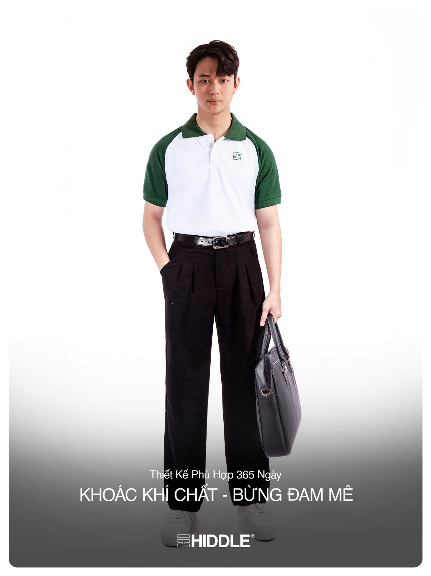 Man wearing a green and white polo shirt with black pants, holding a gray bag on a white background.