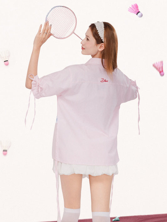 Woman in a pink shirt with a brand logo, holding a badminton racket on a white background