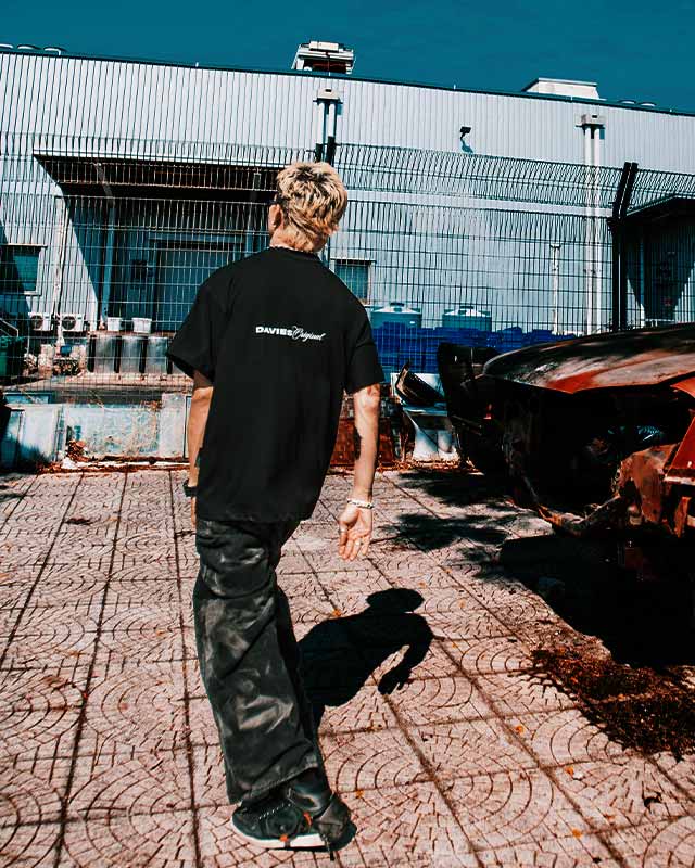 Person wearing a black t-shirt with a brand logo, standing in front of a building with a pool.