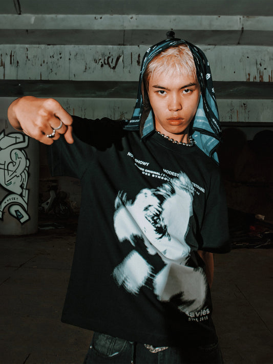 Person wearing a black t-shirt with a graphic design, standing against a concrete wall.