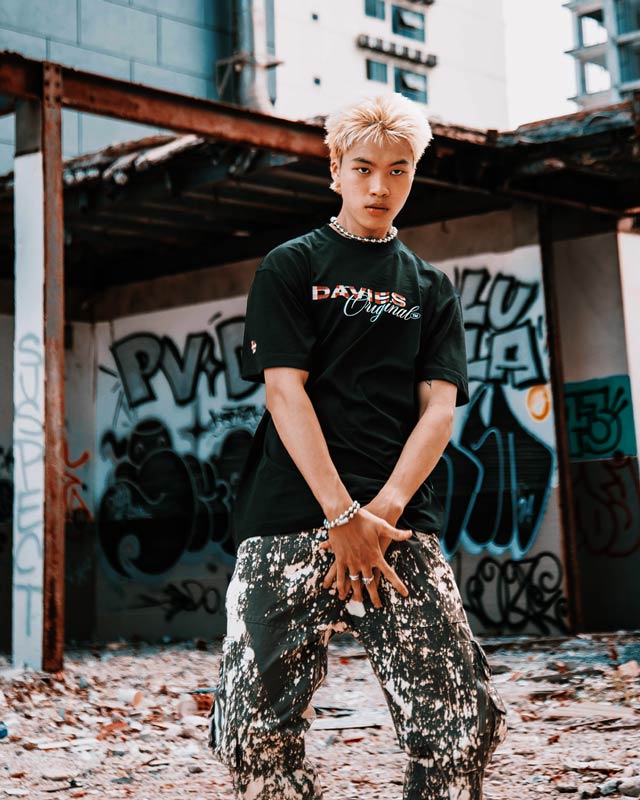 Person wearing a black t-shirt with visible branding in an urban setting with graffiti.
