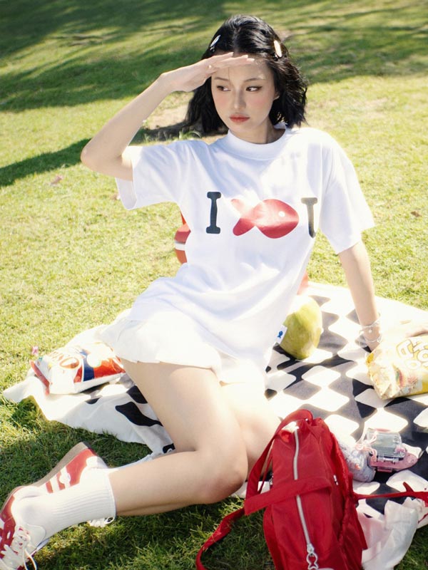 Person sitting on a blanket in a park wearing a white t-shirt with text and graphics.