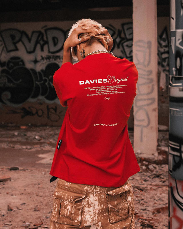 Person wearing a red 'DAVIES Original' shirt in an urban setting with graffiti.