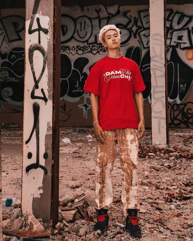 Person wearing a red t-shirt with text, standing in an urban setting with graffiti.