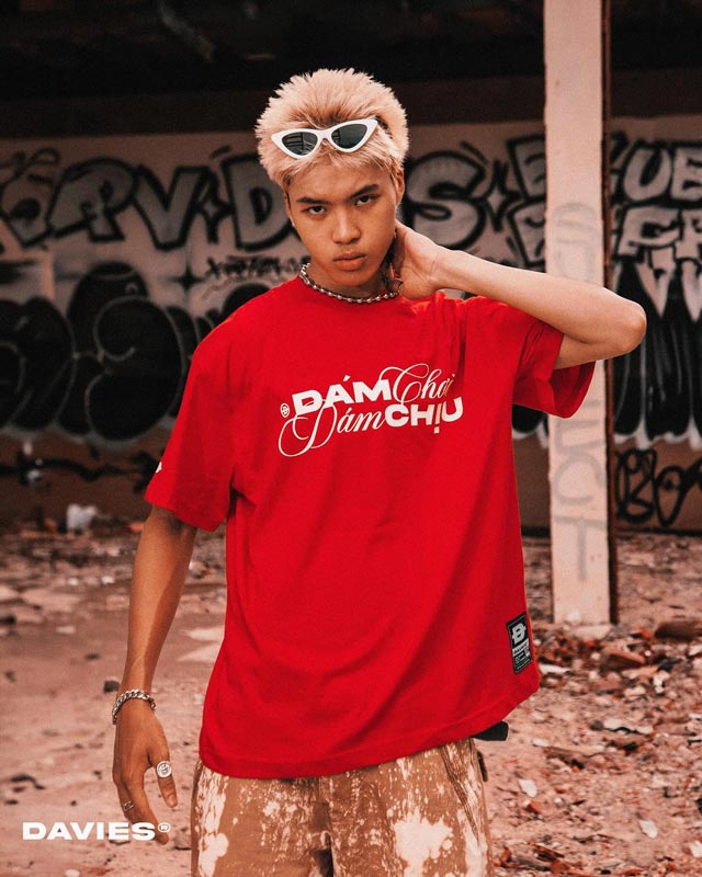 Person wearing a red t-shirt with text, standing in front of a graffiti-covered wall.
