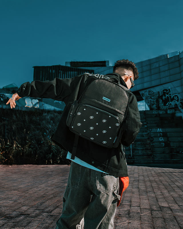 Person wearing a black backpack with white patterns, standing outdoors against a blue sky.