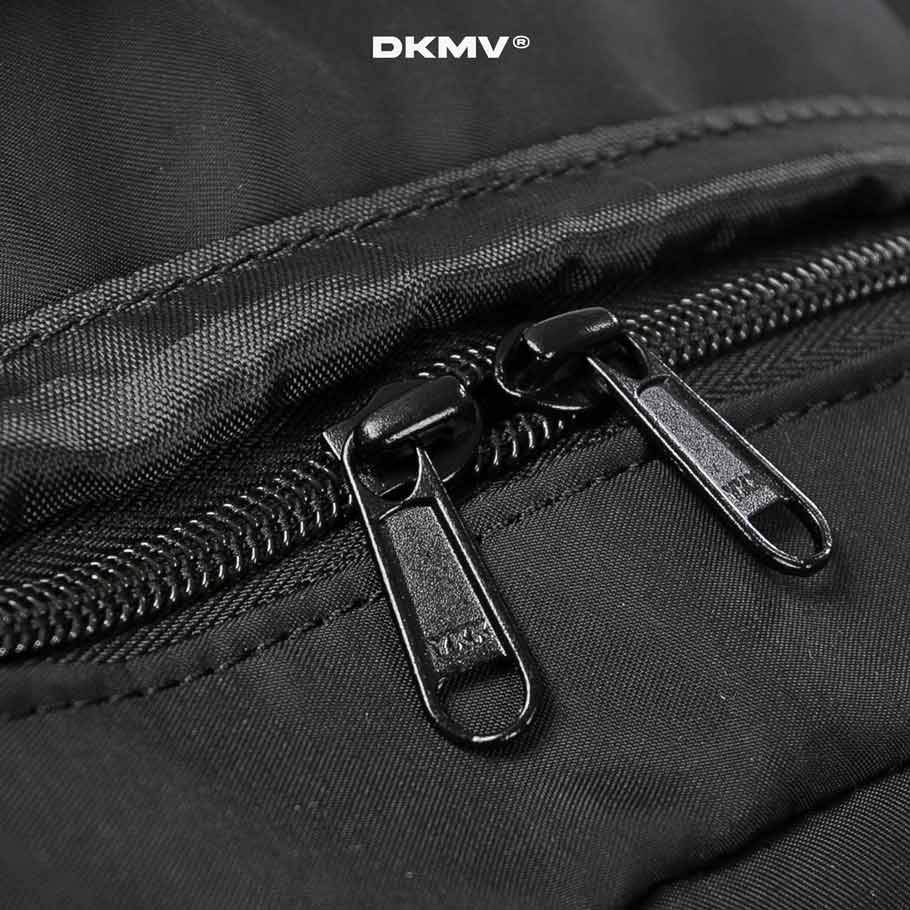 Close-up of a black zipper on a black bag with 'DKMV' branding.