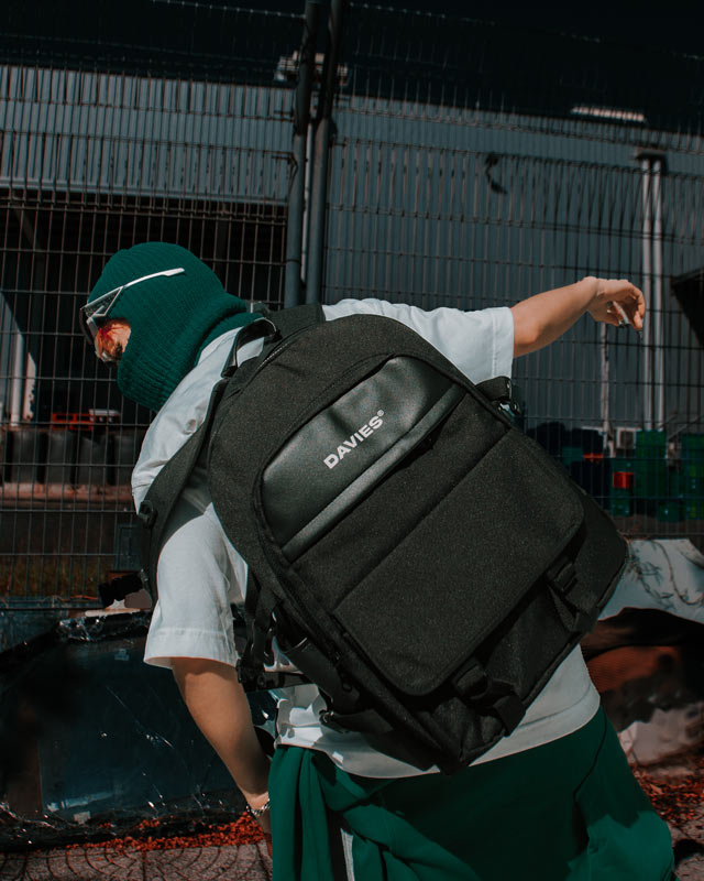 Person wearing a black 'DAVES' backpack in an outdoor setting
