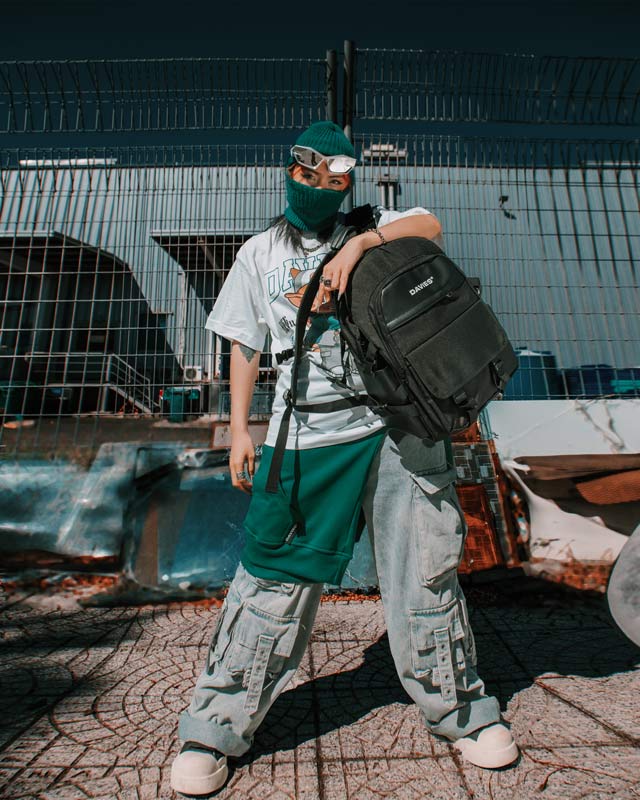 Person wearing a green beanie, face mask, and carrying a black backpack in an urban setting.