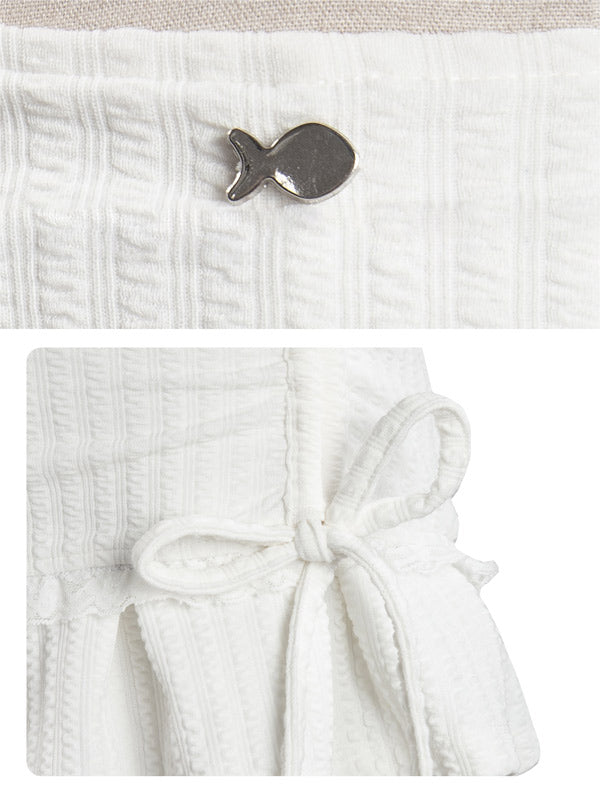 White textured fabric with a small fish-shaped brooch on a beige background