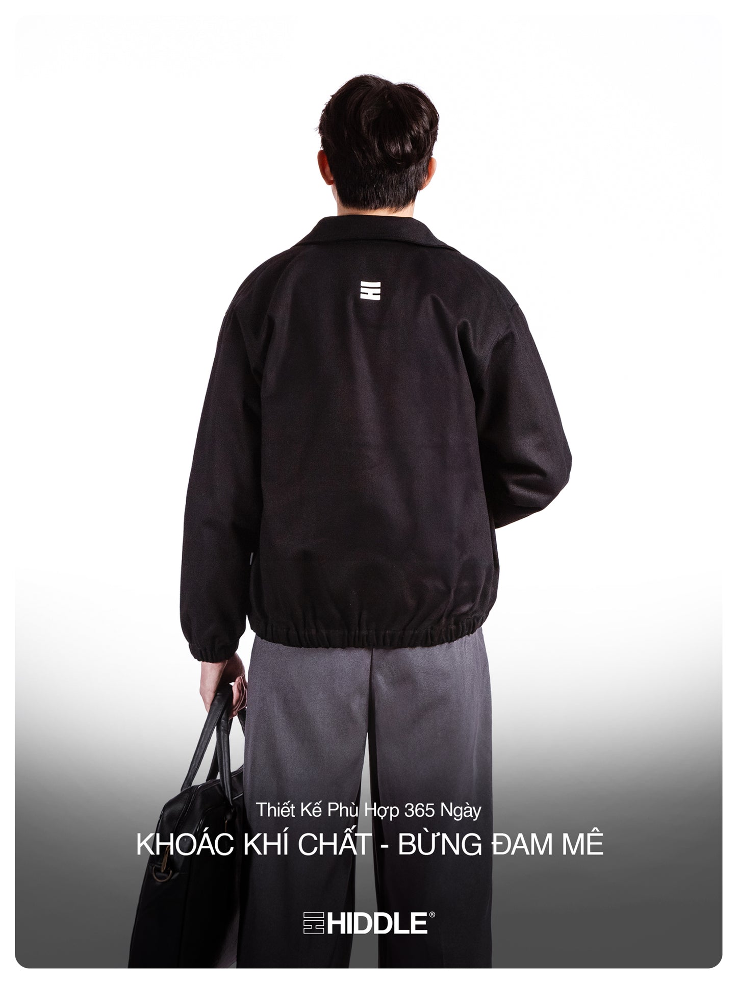 Person wearing a black jacket with a logo on the back, holding a bag.