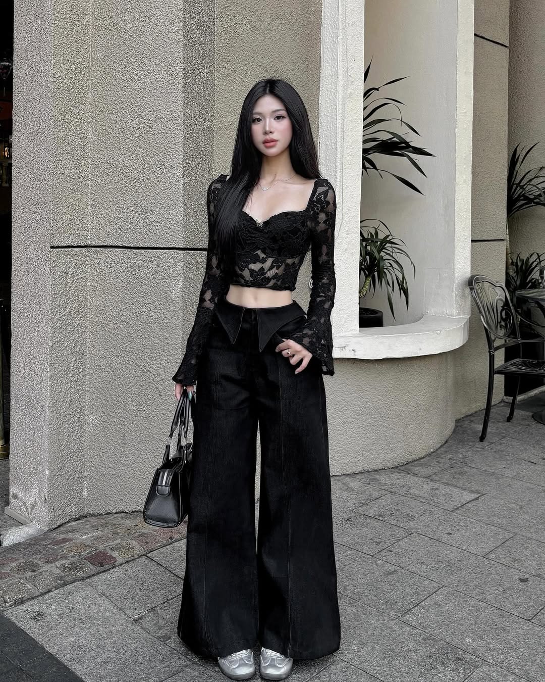 Woman in a black outfit standing outside a building with plants.