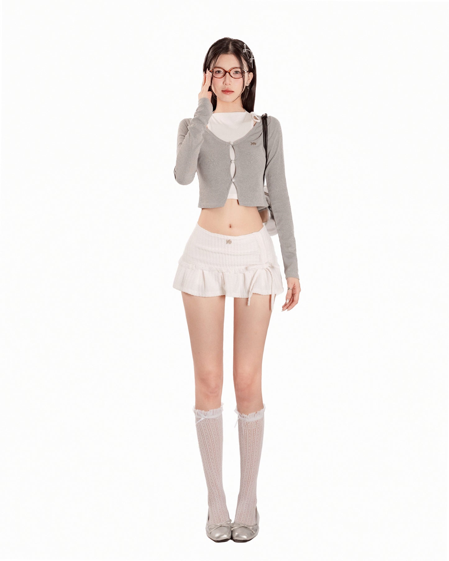 Woman wearing a gray cardigan, white top, and skirt with knee-high socks on a white background