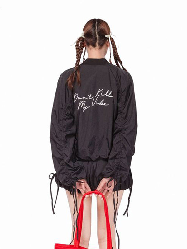 Person wearing a black jacket with text, holding red high-heeled shoes on a white background
