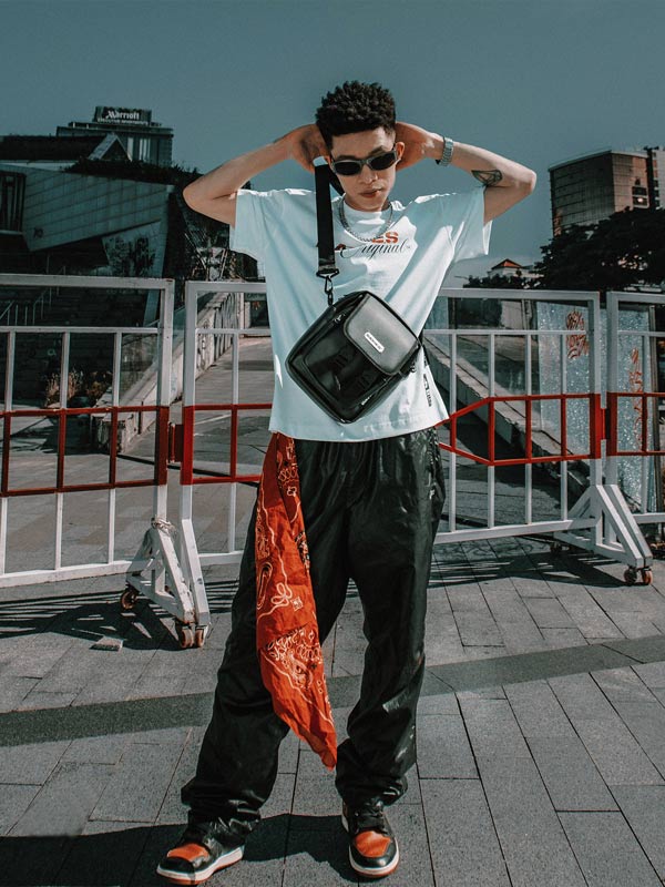 Person wearing a light blue t-shirt with graphics, dark pants, and an orange bandana outdoors.