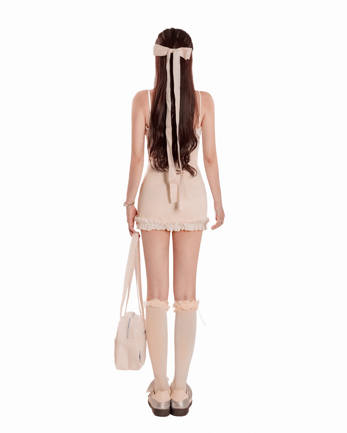 Woman wearing a beige dress with lace details, knee-high socks, and holding a matching handbag on a white background.