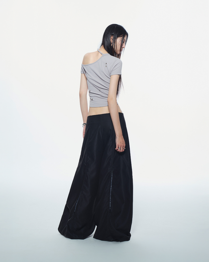 Woman wearing a gray one-shoulder top and black wide-leg pants on a white background