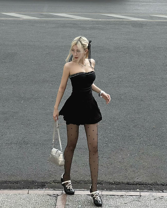 Woman in a black dress and stockings walking on a street.