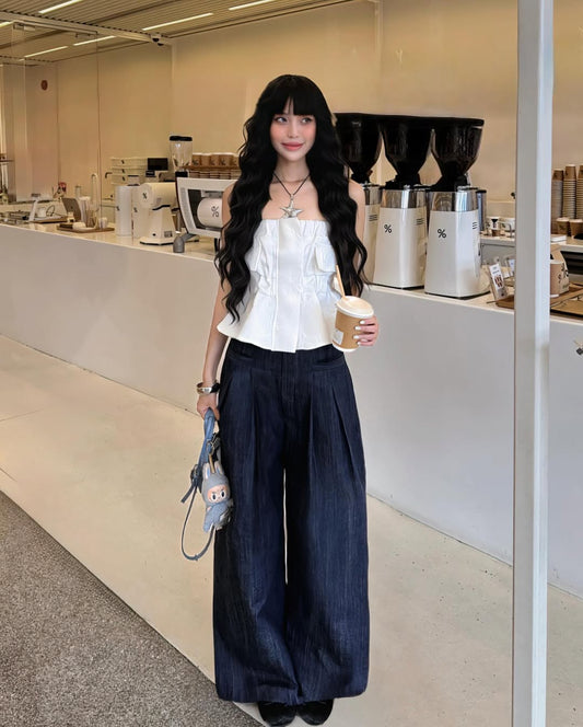 Woman in a white top and dark pants holding a drink in a coffee shop.