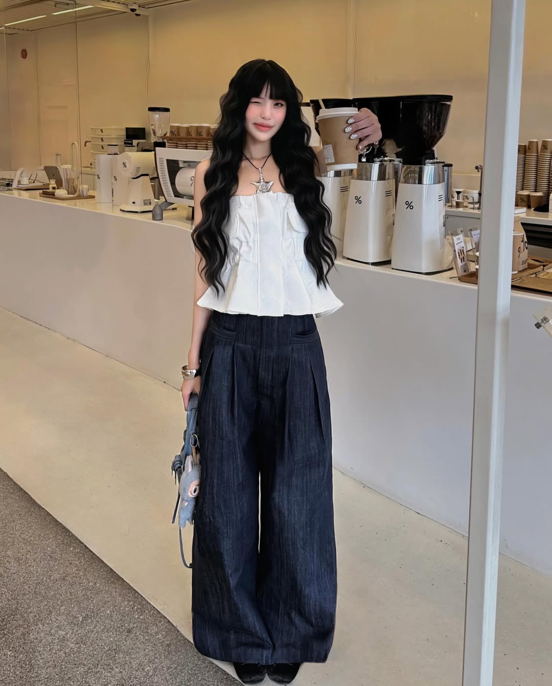 Woman in a white top and dark pants standing in a coffee shop.