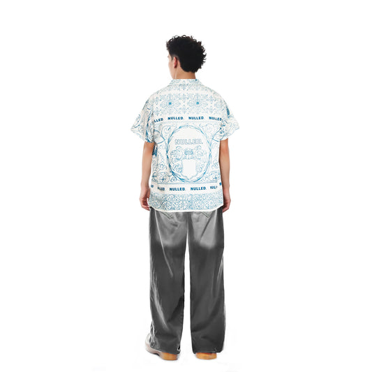 Person wearing a patterned shirt and gray pants on a white background