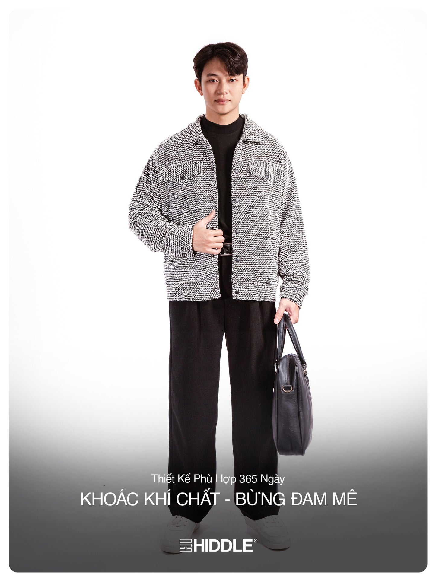 Man wearing a gray jacket and black pants holding a bag on a white background