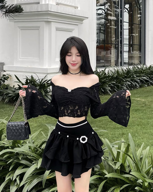 Woman in a black outfit with sheer sleeves standing outdoors.