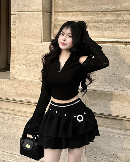 Woman in black outfit with a skirt and top standing against a stone wall.