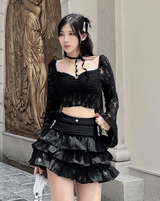Woman in a black outfit standing in front of a stone wall with an angel sculpture.