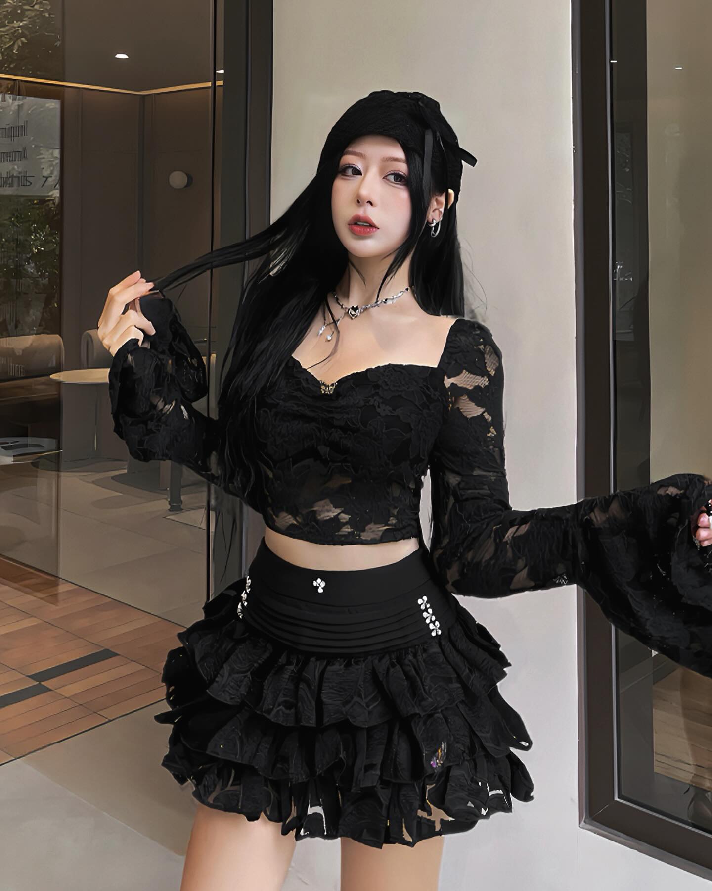 Person wearing a black lace outfit with long sleeves and a skirt, standing indoors.