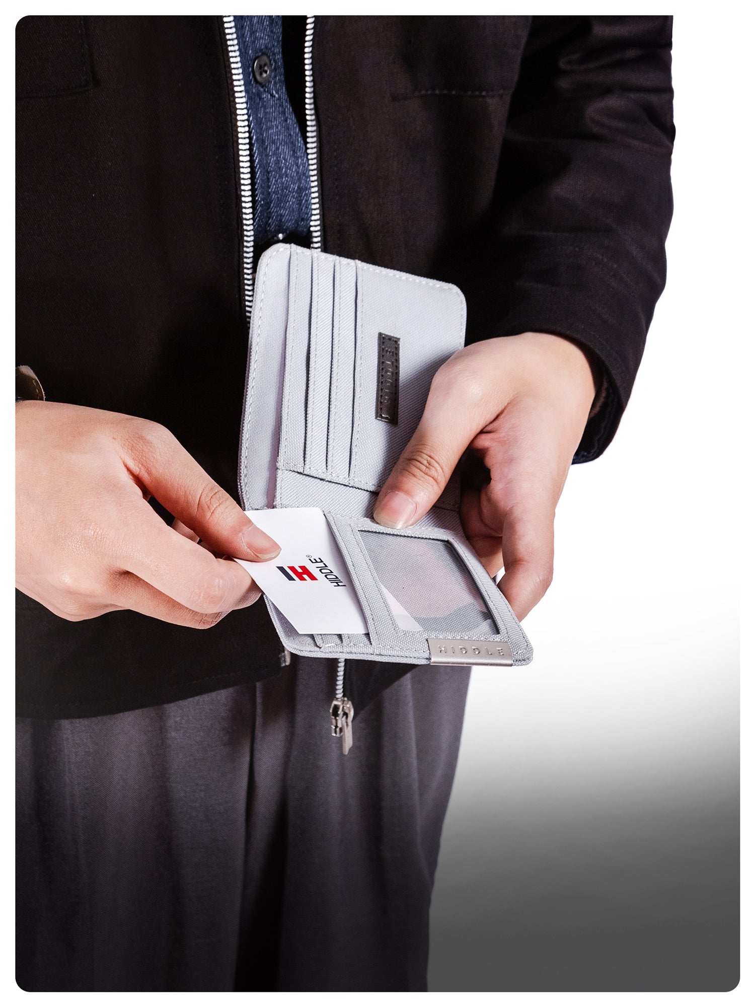 Person holding a gray wallet with a card extracted, wearing a black jacket.