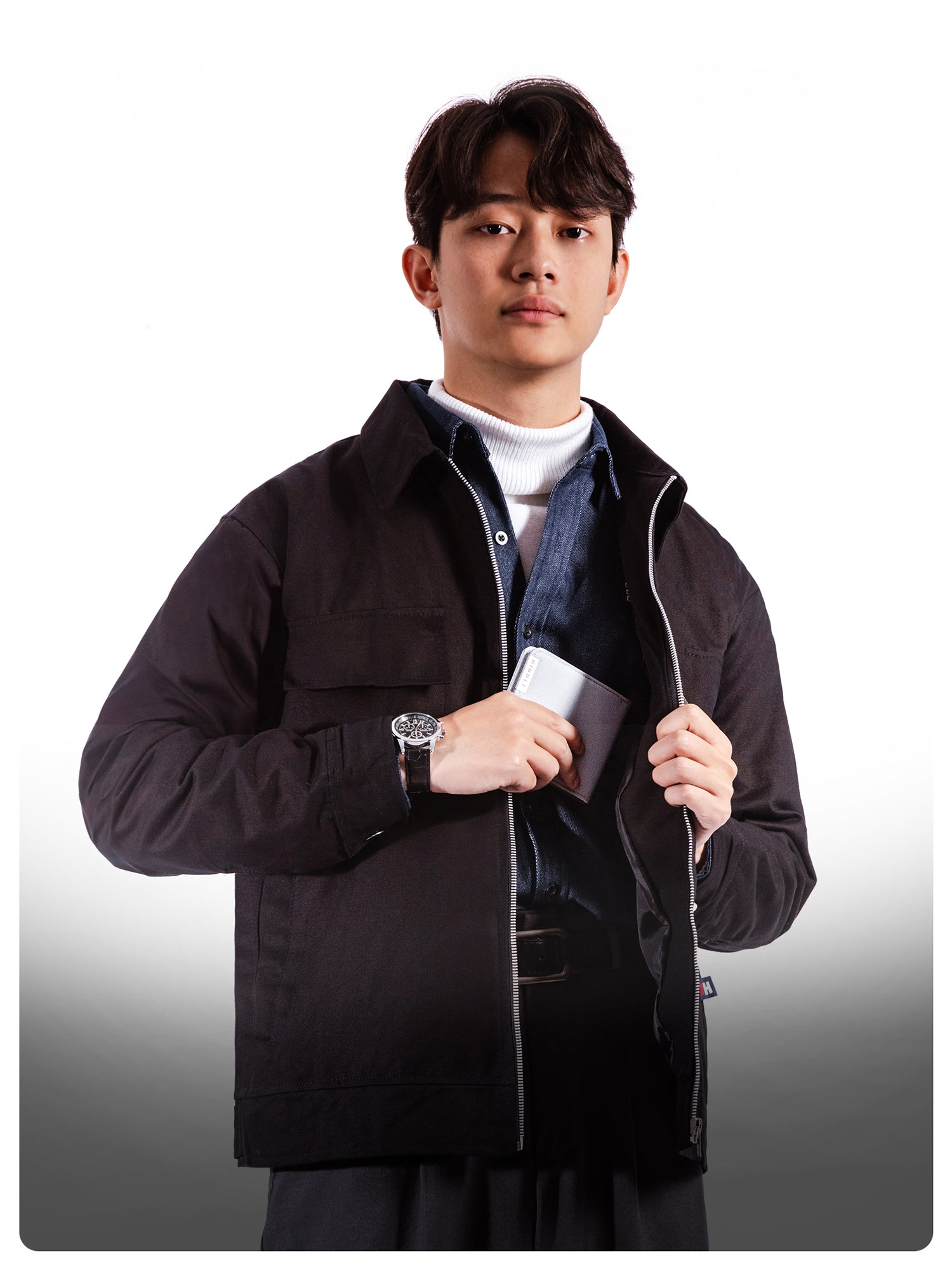 Man wearing a dark jacket holding a phone and wallet on a white background