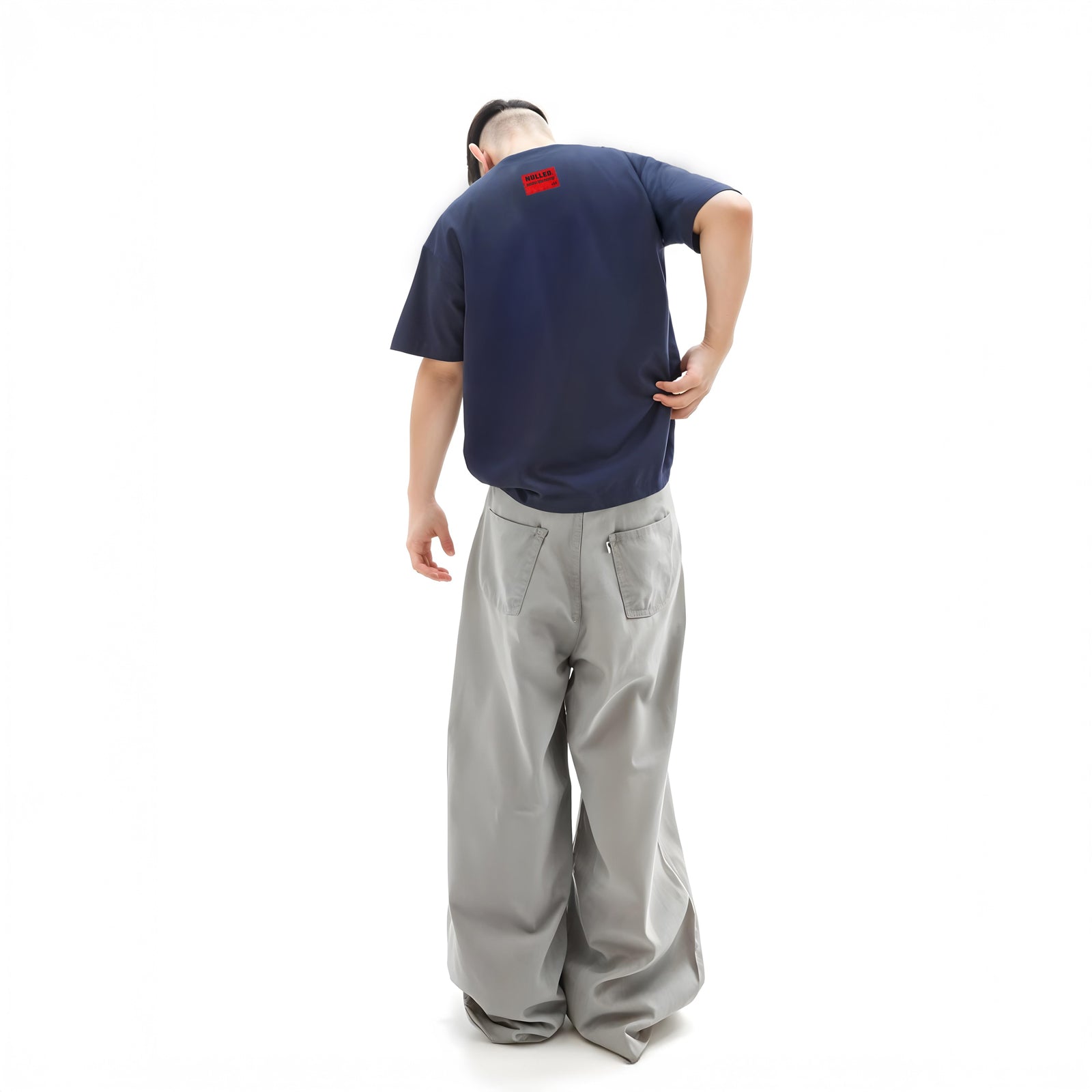 Person wearing a navy blue t-shirt with a red logo and gray pants on a white background