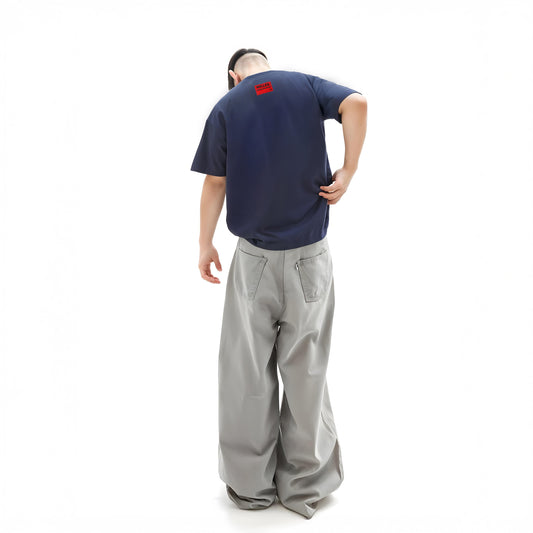 Person wearing a navy blue t-shirt with a red logo and gray pants on a white background