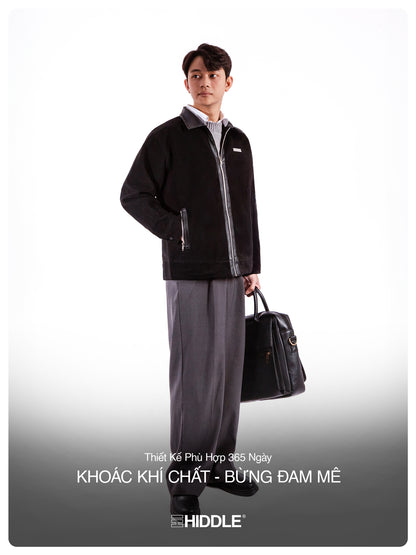 Man holding a black briefcase against a white background, wearing a black jacket and gray pants.